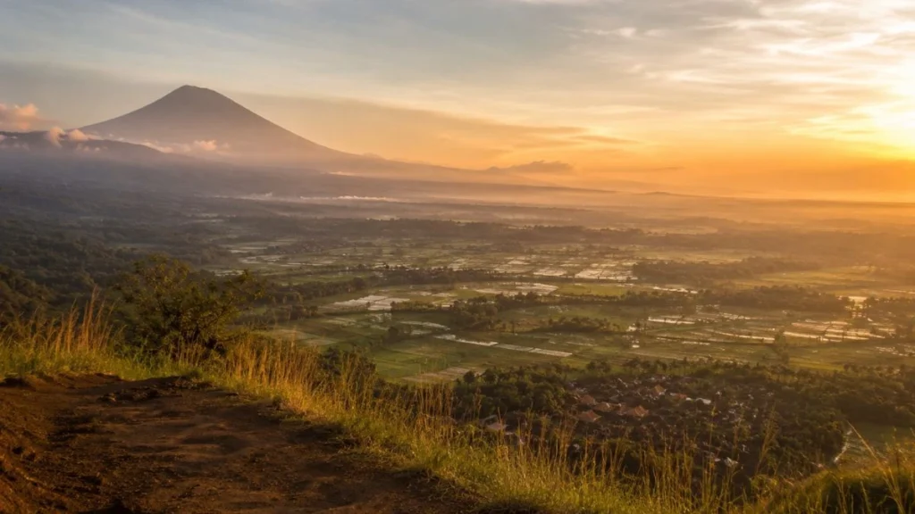 Bali sunrise spots without crowds — Mount Agung silhouette through morning mist from elevated East Bali ridge viewpoint at pre-dawn golden light.